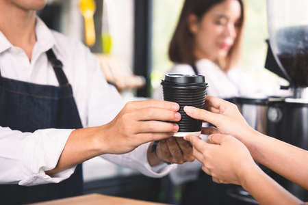 Close up hands customer receive the cup of hot coffee latte from barista. Coffee cafe shop beverage concept.の写真素材