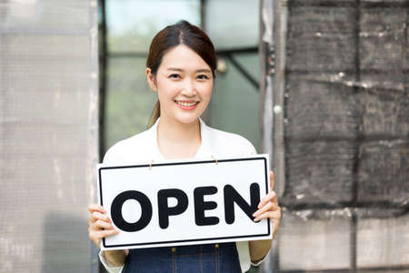 The owner of the tree shop holds a open sign after a long time closed. Cute asian gardener small business open her shop selling small tree for decoration in greenhouse.の写真素材
