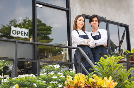 Couple asian barista owner coffee shop standing welcome the customer. Cheerful two young barista man and woman in apron serving cup of hot coffee in cafe.の写真素材