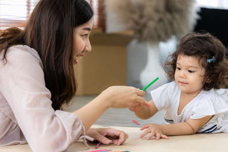 Mother and daughter drawing and coloring with colored pencils lying down on the floor. Happy family moment in the house.Art Activity in kindergarten.の写真素材