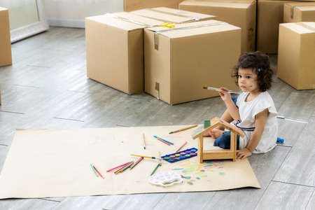 Cute daughter painting coloring with watercolor on the wooden house mock up. Sitting on the floor in...