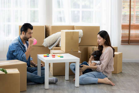 Parents and daughters play with pink balloon sitting on the floor in the living room at home. The...