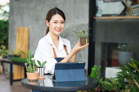 Young cute asian woman working in house plant. Asian female gardener using a tablet to record and capture the growth of trees in greenhouse. Startup small business work from home concept.の写真素材