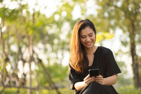 Asian woman mature using cell phone in public park. Adult female holding cell phone with beautiful...