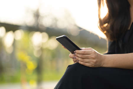 Close up hands woman using cell phone in public park. Adult female holding cell phone with beautiful sun light.の写真素材
