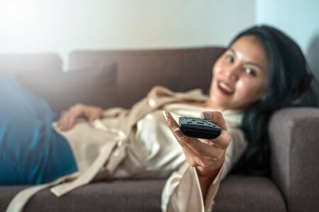 Asian woman holding a tv remote on a sofaの写真素材