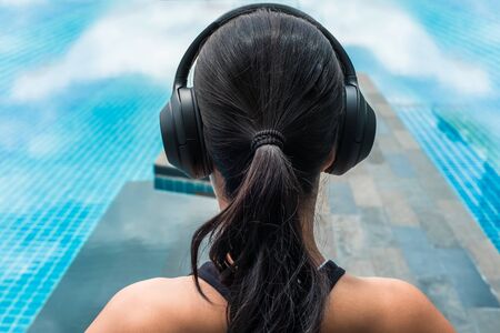 Woman listening music with headphones closed to a pool. Relaxing meditation conceptの写真素材