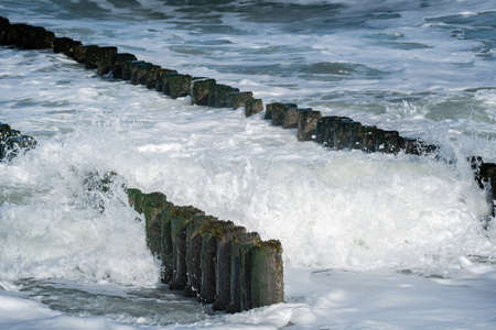Breaking waves and wooden breakwater poles close-up