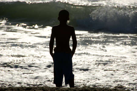 Boy watching waves at the beach at sunriseの写真素材