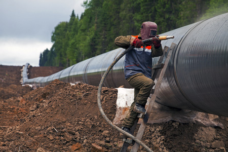 Worker using a sandblaster cleans tubing pipe before insulation