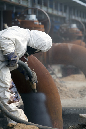 Worker in protective equipment cleans the metal construction before painting themの写真素材