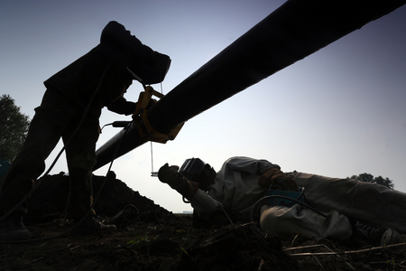 Silhouettes of two workers welding a pipeの写真素材