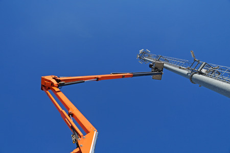 Hydraulic mobile construction platform elevated towards a blue sky with metal pole with street lampの写真素材