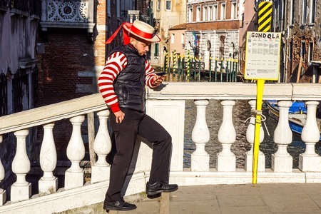 VENICE, ITALY- DECEMBER 2016 Unidentified gondolier using a mobile phone while waiting for clients near a Venetian canal .Gondola is a major mode of touristic transport in Venice, Italyのeditorial素材