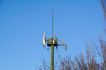 Steel telecommunication tower with antennas over blue sky and treesの写真素材