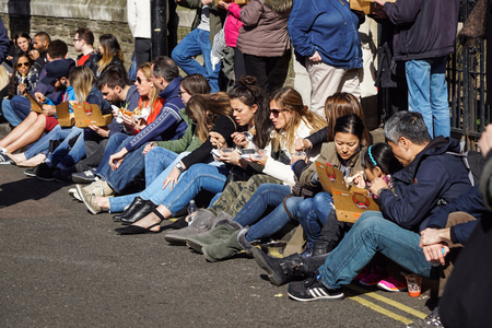 LONDON , APRIL 23 2017: Unidentified A group of people eat a sandwich sitting down the street....