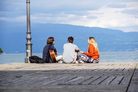 GARDA LAKE, ITALY 20 may 2017 Friends group playing guitar in sunset pier at dusk .のeditorial素材