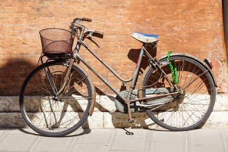 An old, rusty white bicycle with a basket leaning against a grungy wall in Italy.の写真素材