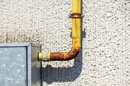 Old water metal pipes fixed with brackets in front of a plaster wall with metal box for water meterの写真素材