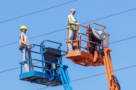 Hydraulic mobile construction platform elevated towards a blue sky with false construction workers . dummy man .の写真素材