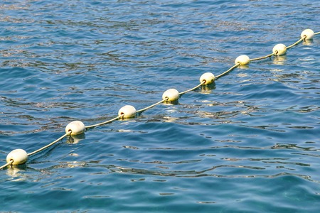 Line of yellow buoys against the blue sea. Restriction on open water. Glare and ripples on the water