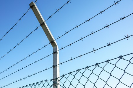 Coiled razor wire with its sharp steel barbs on top of a mesh perimeter fence ensuring safety and...