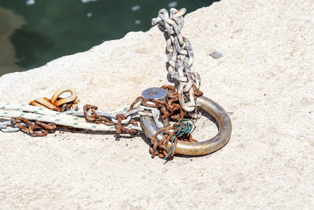Old metal rusty mooring bollard with a chainの写真素材