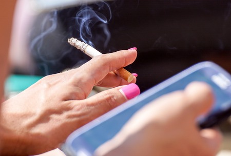 young stylish woman at phone on the beach smoking cigarette outdoors