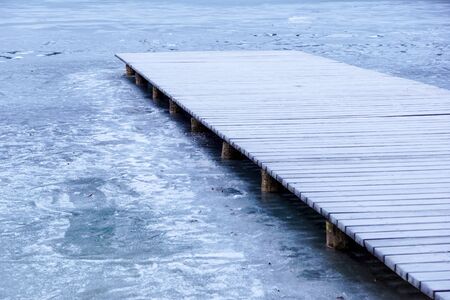Mole pier on the lake. Wooden bridge in forest in winter time with blue frozen lake. Lake for...