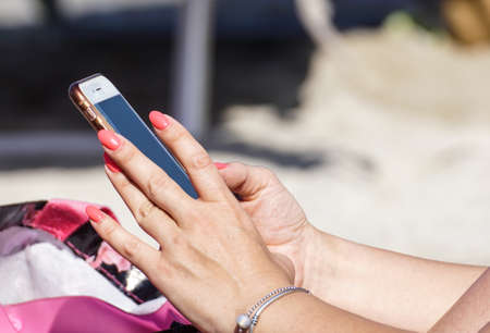 Blonde in a summer hat uses a smartphone near the seaの写真素材