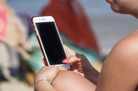 Blonde in a summer hat uses a smartphone near the seaの写真素材