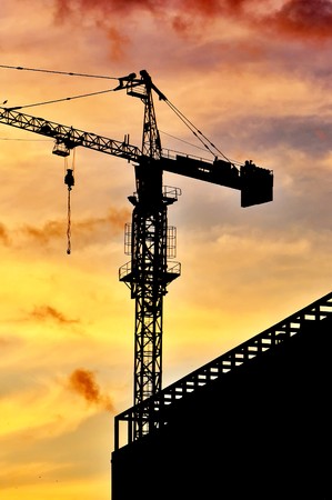 Dark silhouette of a construction crane at dusk, against warm orange sky.の写真素材