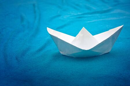 Small white paper ship over a blue background. の写真素材