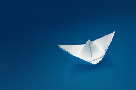 Small white paper ship over a blue background.の写真素材