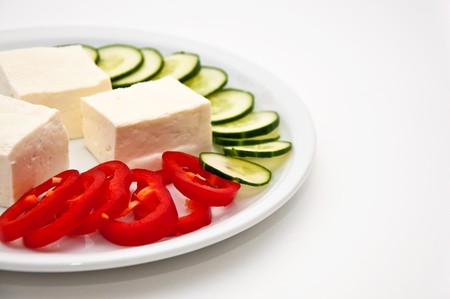 Fresh and tasty goat cheese with cucumber and  paprika served on a white plate.の写真素材