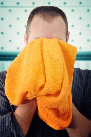 Man is wipeing his face with an ornage towel in a bathroomの写真素材