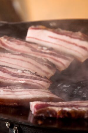Tasty red bacon slices grilling on a plate.