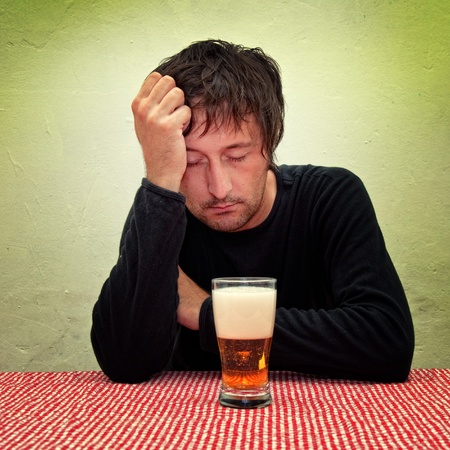 Drunk man at the pub table with a glass of cold, light beer.の写真素材