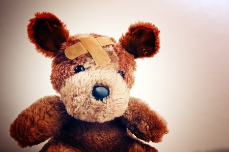 Cute little teddy bear with plaster on his head over a white backgroundの写真素材