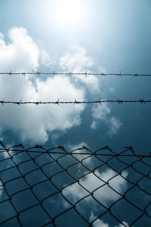 Barbed wire fence against a blue sky with cloudsの写真素材
