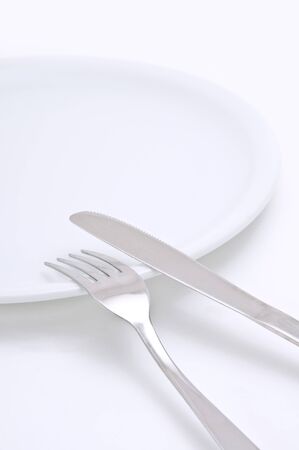 Kitchen knife and a fork and a plate, beautiful silverware on a white background. Image is taken with selective focus and very shallow depth of field.の写真素材