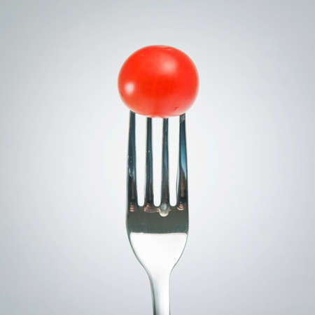 Tasty red cherry tomato on a beautiful silver forkの写真素材