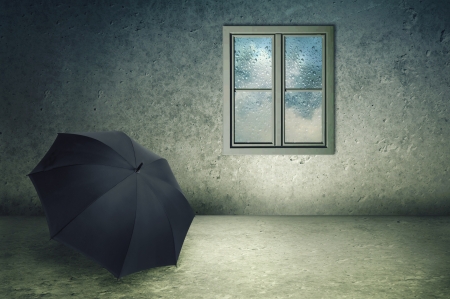 Forgotten black umbrella in a cold concrete room, rain drops on window pane.の写真素材