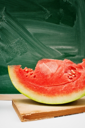 Tasty watermelon  and a book in front of the green chalkboard, back to school conceptの写真素材
