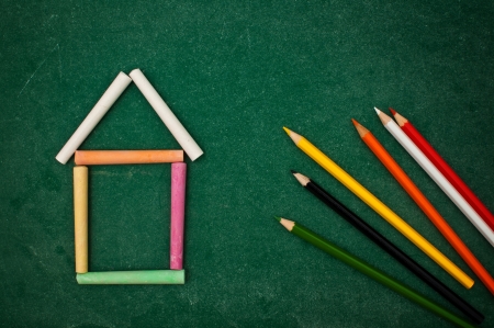 Back to school, handwritten letters on a green chalkboard. Colorful chalks forming the shape of a house or a school building.の写真素材
