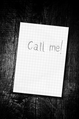 Call me, reminder paper note over a wooden background, black and white image.の写真素材