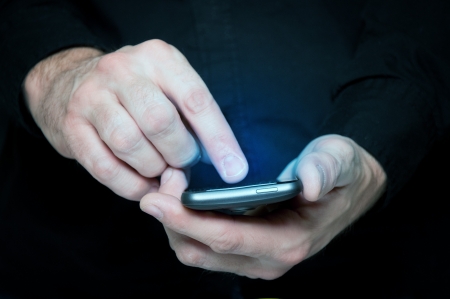 Man in black shirt is typing a text message on his smartphone, close up image, focus on hands and the phone device.の写真素材