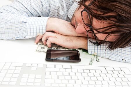 Hardworking businessman fall asleep at the office desk, his mobile phone and some money in front of...