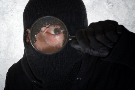 Burglar concept, thief with balaclava holding magnifying glassの写真素材