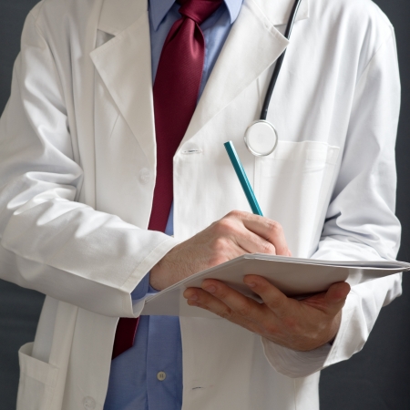Male doctor in white coat is writing notes in white notebook.の写真素材